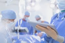 Chirurgien portant des gants en caoutchouc, utilisant une tablette numérique en salle d'opération — Photo de stock