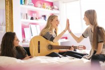 Teenage girls with guitar high fiving on bed — Stock Photo