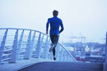 Male runner running on urban footbridge at dawn — Stock Photo