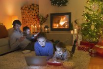 Родина розслабляється, використовуючи ноутбук, цифровий планшет і мобільний телефон в навколишній різдвяній вітальні — стокове фото