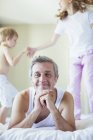 Children jumping on bed around father — Stock Photo
