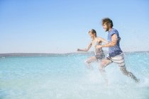 Casal correndo na água na praia — Fotografia de Stock