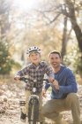 Retrato sonriente padre enseñando hijo a montar en bicicleta en el bosque - foto de stock