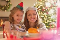 Портрет улыбающейся матери и дочери в шляпе эльфа и бумажной короне за праздничным столом — стоковое фото