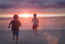Хлопчик і дівчинка брат і сестра на спокійному пляжі заходу сонця з драматичним небом — стокове фото