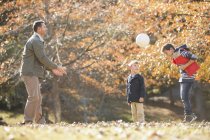 Padre e hijos jugando fútbol en el parque de otoño - foto de stock