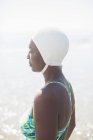 Вид сбоку застенчивой женщины в купальном костюме и шапке — стоковое фото