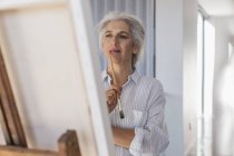Pensive mature woman painting at easel — Stock Photo