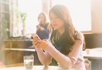 Mujer mensajes de texto con teléfono celular en la mesa de la cafetería - foto de stock