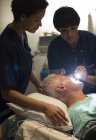Female doctor examining senior patient with flashlight in intensive care unit — Stock Photo