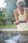 Mulher bebendo água da piscina em sua mão — Fotografia de Stock