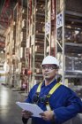 Serious worker with clipboard in distribution warehouse — Stock Photo