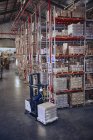 Carrello elevatore operante operaio che muove scatole di cartone vicino agli scaffali del magazzino di distribuzione — Foto stock