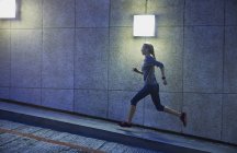Female runner running ascending illuminated urban ramp — Stock Photo