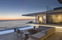 Beleuchtete moderne, luxuriöse Wohnvitrine Außenterrasse mit Sofa und Pool mit Meerblick in der Abenddämmerung — Stockfoto