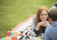 Feliz joven pareja relajándose en manta en el parque - foto de stock
