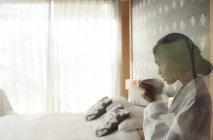 Mujer en albornoz bebiendo café en el dormitorio - foto de stock