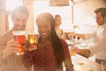 Retrato sonriente pareja tostando vasos de cerveza en el bar - foto de stock