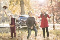 Boys and girl throwing autumn leaves overhead in woods — Stock Photo