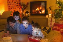 Familia comer palomitas de maíz y ver vídeo en el ordenador portátil en el ambiente sala de estar de Navidad con chimenea - foto de stock
