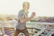 Determined male runner running on sunny urban footbridge at sunrise — Stock Photo