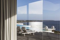 Ventana vista al soleado y moderno patio de lujo con piscina infinita y vista al mar - foto de stock