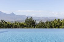 Tranquillo lusso piscina a sfioro con soleggiata vista sulle montagne — Foto stock