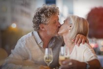 Ласковая пожилая пара целуется, пьет белое вино в кафе на тротуаре — стоковое фото