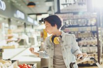 Young woman with headphones browsing, grocery shopping in market — Stock Photo