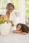 Grandmother and granddaughter unpacking groceries in kitchen — Stock Photo