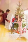 Parents giving large Christmas gift to daughter in living room next to Christmas tree — Stock Photo