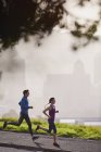 Corredor pareja corriendo en la soleada acera urbana - foto de stock