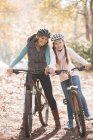 Portrait smiling mother and daughter on mountain bikes in woods — Stock Photo