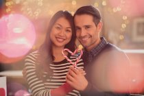 Portrait smiling couple holding heart-shape candy canes — Stock Photo
