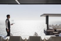 Camarero sirviendo champán en cabaña con vistas al océano - foto de stock