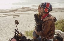 Pareja joven abrazándose a la motocicleta mirando al océano - foto de stock
