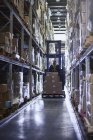 Empilhadeira de mão de obra com caixas de papelão no corredor do armazém de distribuição — Fotografia de Stock