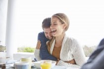 Affectionate couple hugging and laughing at breakfast on patio — Stock Photo
