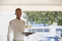 Портрет улыбающегося официанта, подающего белое вино на подносе в ресторане — стоковое фото