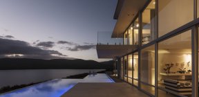 Спокойная современная витрина роскошного дома с подсвеченным бассейном и видом на сумерки океана — стоковое фото