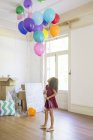 Young girl holding balloons in living space — Stock Photo