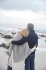 Heiteres, liebevolles Paar, das sich am Winterstrand umarmt und auf das Meer blickt — Stockfoto