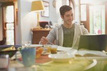 Young man college student using laptop studying at breakfast — Stock Photo