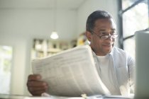 Hombre mayor con periódico usando portátil - foto de stock