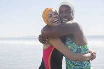 Mulheres entusiasmadas abraçando em roupas de banho e bonés — Fotografia de Stock