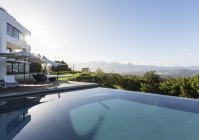 Tranquille, maison ensoleillée vitrine extérieure avec piscine à débordement et vue sur la montagne sous le ciel bleu — Photo de stock