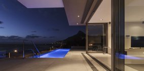 Illuminated blue lap swimming pool outside modern luxury home showcase exterior at night — Stock Photo