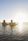 Couple in lawn chairs in infinity pool overlooking ocean — Stock Photo