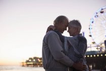 Старша пара обіймається на пляжі на заході сонця — стокове фото