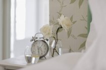 Rose blanche, réveil et verre d'eau sur la table de chevet — Photo de stock